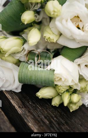 Two golden wedding rings resting on the green stems of a white bridal bouquet Stock Photo