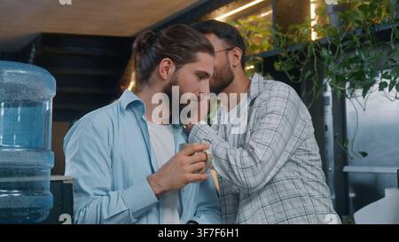 Two diversity men Caucasian business man relax drinking coffee Indian male talking secret on ear amazing secrecy information break pause startup space Stock Photo
