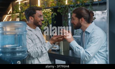 Arabian man near water cooler in office two diversity business men friends guys businessmen discussing amazing news happy laughing excited talk Stock Photo