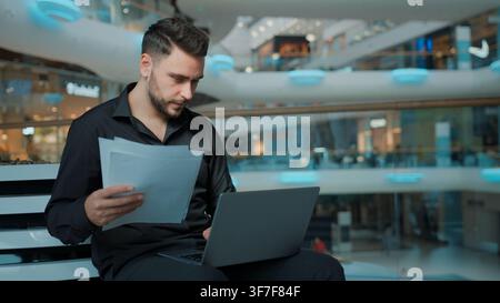 Concentrated Caucasian male businessman working with laptop and papers data managing paperwork in business center man guy entrepreneur work with Stock Photo