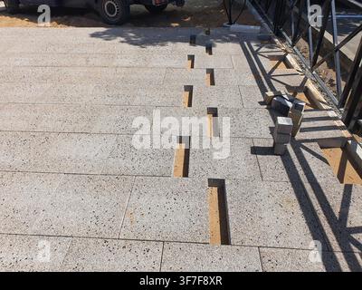 Outdoor construction site showing a partially completed paved walkway or patio area. Large rectangular grey granite or stone tiles are laid in a Stock Photo
