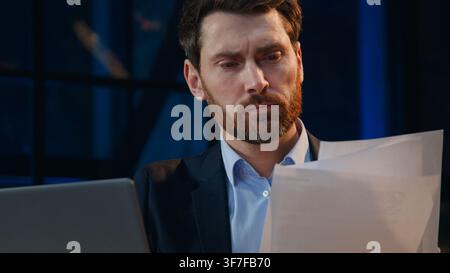 Close up serious Caucasian middle-aged business man with computer and papers at evening company businessman male corporate leader working with laptop Stock Photo