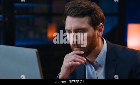 Concentrated Caucasian middle-aged business man working with computer thinking at evening pensive looking in desktop monitor adult mature male Stock Photo