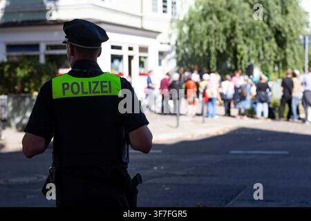 A uniformed police officer in focus observes a blurred crowd in a public space. Stock Photo