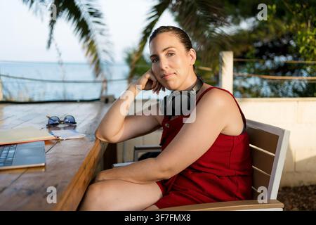focused young digital nomad woman doing remote work on laptop at outdoor terrace cafe with headphones during an online meeting, nomad freelance Stock Photo