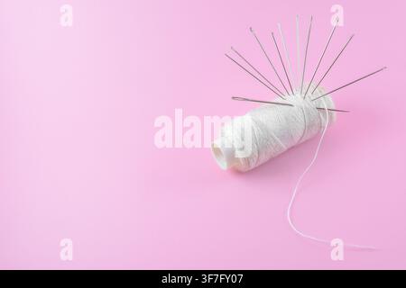 Traditional Sewing tools, needles and white thread isolated pink background Stock Photo