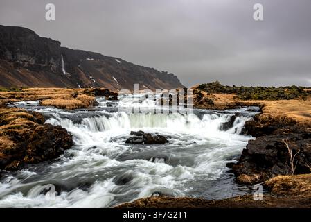Spectacular Icelandic panorama featuring a series of rushing rapids and foaming waterfalls in the foreground. The river flows through dark rocks and g Stock Photo