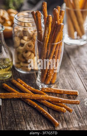 Close-up of salted pretzel sticks arranged on a weathered wooden table with a glass jar in the background, evoking a cozy, rustic snack scene perfect Stock Photo