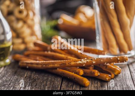Close-up of salted pretzel sticks arranged on a weathered wooden table with a glass jar in the background, evoking a cozy, rustic snack scene perfect Stock Photo