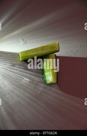 Close-up commercial shot of two fresh raw green cucumber pieces arranged on a textured dark background. Ideal for concepts related to healthy eating, clean diet, organic vegetables, vegetarian food, hydration, and culinary ingredients. Stock Photo