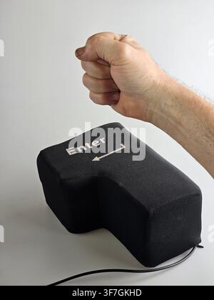 Clenched human fist raised beside an oversized soft USB Enter key on a white background, a humorous concept of computer frustration, workplace pressur Stock Photo