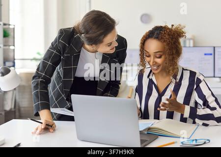 Smiling businesswomen discussing ideas at laptop in bright office workspace Stock Photo