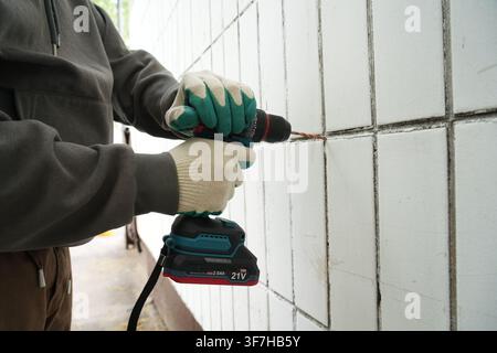 Using teal cordless brushless drill on tiled wall Stock Photo