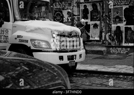Snow-capped truck idles beneath torn fashion posters and graffiti on a gritty corner in NYC Stock Photo