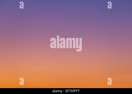 A clear sky displays a smooth color gradient from deep violet to vibrant orange. This cloudless, minimalist scene is ideal for backgrounds and creativ Stock Photo