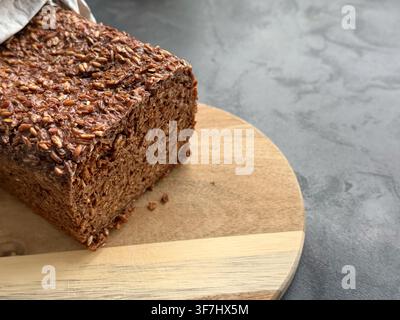 Freshly baked whole grain seeds bread loaf displayed on a wooden cutting board with a textured gray background  Stock Photo