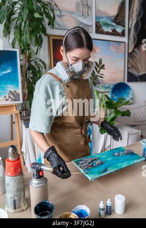 Focused professional woman crafter in safety gear working with epoxy resin creating liquid art. Stock Photo