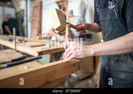 Hardworking carpenter in restoration workshop renovating wooden frame with mallet and chisel tools. Stock Photo