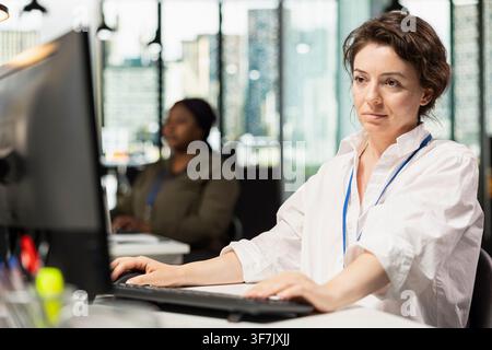 Smiling IT worker using PC at office desk, working with software development programming languages. Happy engineer using computer in startup company to do code testing and quality assurance Stock Photo
