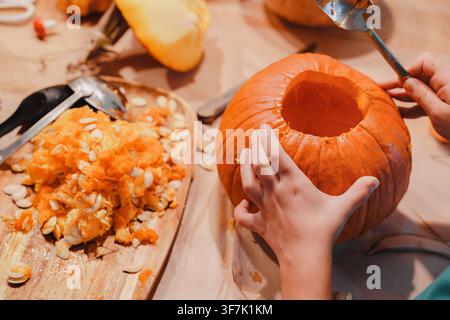 Child cleans the inside of an open pumpkin with a spoon, removing pulp and seeds as the first step in preparing a Halloween jack-o-lantern, Halloween Stock Photo