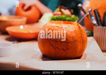 Orange pumpkin with a carved jack-o-lantern face sits, decorates and displays on a table, Halloween celebration, seasonal home decor. Stock Photo