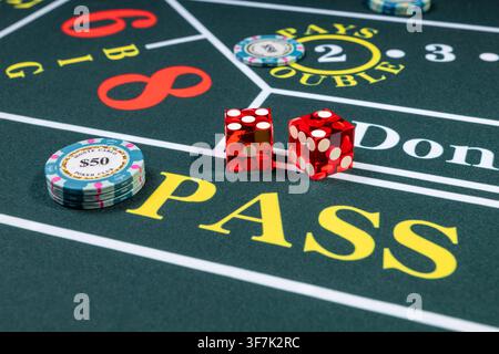 ST. CLOUD, MINNESOTA, UNITED STATES — JULY 27, 2026: Two translucent red dice and several casino chips are arranged on the Pass and other sections of Stock Photo