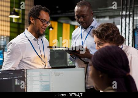 Engineering team doing brainstorming, using computer in workplace to do maintenance on neural networks. Tech startup office teamworking colleagues using AI machine learning systems on PC Stock Photo