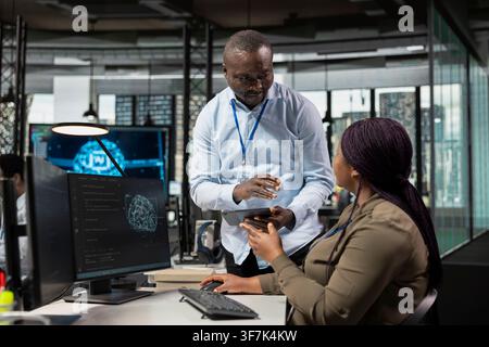 Manager supervising IT staff member in office automating repetitive business workflows using artificial intelligence tech. Team leader overseeing woman refining deep learning computational models Stock Photo