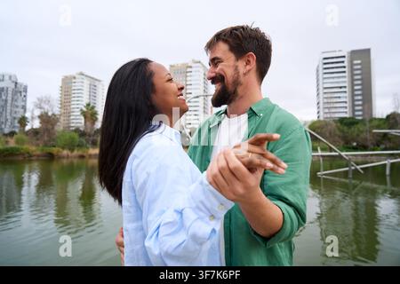 Happy multiracial couple dancing by lake in city park. Stock Photo