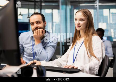 Senior team leader mentoring junior dev at desk in office, teaching best coding practices. Tech company IT professional guiding female developer intern through project tasks Stock Photo