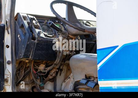 View of the decayed interior of an old, abandoned truck, the seat, steering wheel, dashboard, and wires exposed falling along the steering wheel colum Stock Photo
