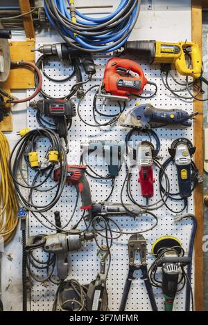 Various electric power tools including drills, circular sanders, jig saw hanging on white pegboard in home garage workshop, Quebec, Canada Stock Photo
