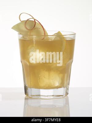 Yellow cocktail on ice cube cubes against a white background, half an apple slice and half a slice of lemon as a garnish, studio shot Stock Photo
