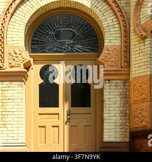 Yellow with keyhole-shaped windows, ornate iron transom and decorative brick and terracotta surround on a historic Chicago building. Stock Photo