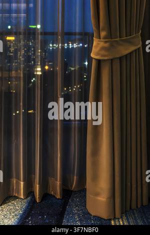 Hotel room view through curtain illuminated city scenery, Pattaya, Thailand Stock Photo