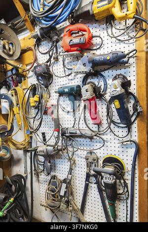 Various electric power tools including drills, circular sanders, jig saw hanging on white pegboard in home garage workshop, Quebec, Canada Stock Photo