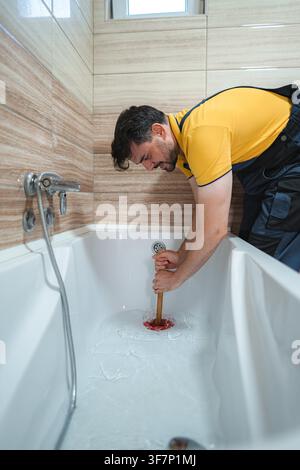 Plumber working to unclog a blocked bathtub drain using a force cup plunger Stock Photo