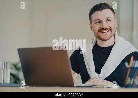 Young man writes notes beside laptop while working at desk in bright home office Stock Photo