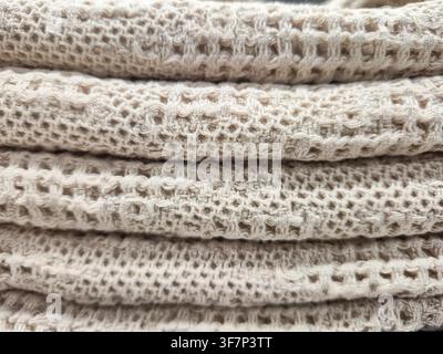 A detailed macro shot showcases the intricate weave and soft texture of stacked beige textile, highlighting its breathable, open-knit structure Stock Photo