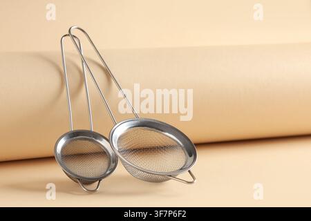 Two stainless steel mesh strainers with long handles for kitchen and cooking use on a beige background Stock Photo