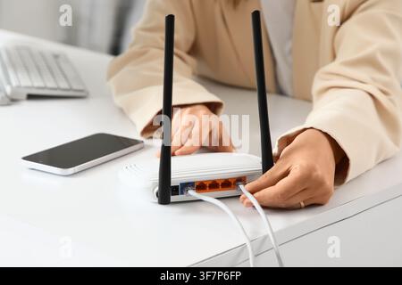 Woman connecting ethernet cable to a white wireless router on a desk with a smartphone and keyboard, a smartphone and a computer keyboard are also vis Stock Photo