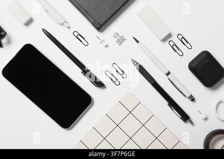 Flat lay of black and white office supplies with a smartphone, notebook, pens, and paper clips on a clean background Stock Photo