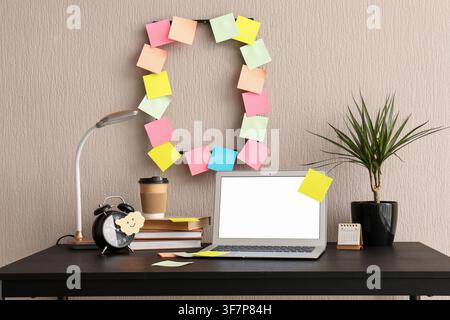 Workplace with blank laptop, sticky notes and alarm clock in office Stock Photo