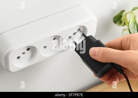 Hand plugging a black charger into a white european power strip on a wall, electricity and energy Stock Photo