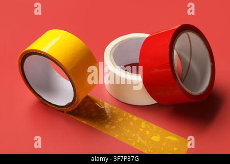 Three rolls of colorful adhesive tape including yellow white and red on a vibrant red background for packaging and repair Stock Photo