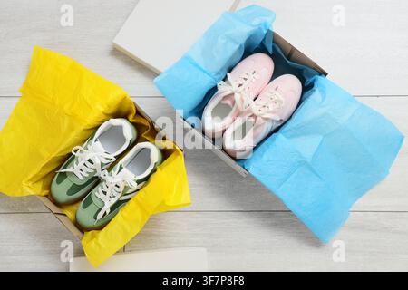 New green and pink sneakers in open shoeboxes with colorful tissue paper on a light wooden floor, top view Stock Photo