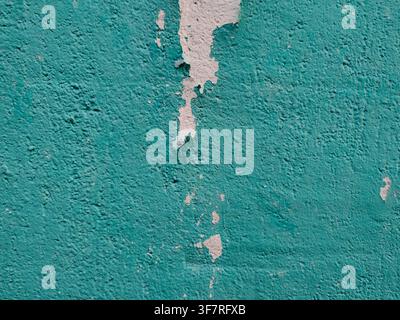 A textured turquoise painted wall features a prominent vertical strip of peeling paint exposing white plaster beneath. Stock Photo