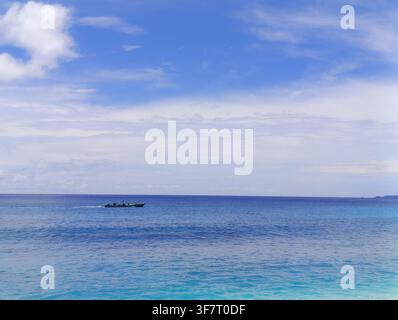 Small boat floating on calm blue sea beneath a bright sky with soft clouds and a distant horizon. Stock Photo