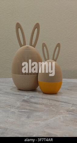 Big beige and small yellow 3D-printed Easter eggs with textured bunny ears, a creative holiday decoration and unique gift idea Stock Photo