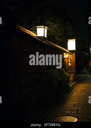Traditional wooden machiya houses lit by paper lanterns along a narrow alley at night in Higashiyama, Kyoto, Japan Stock Photo